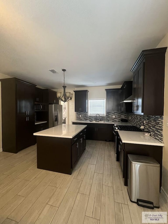 kitchen with appliances with stainless steel finishes, light hardwood / wood-style flooring, a notable chandelier, a kitchen island, and hanging light fixtures