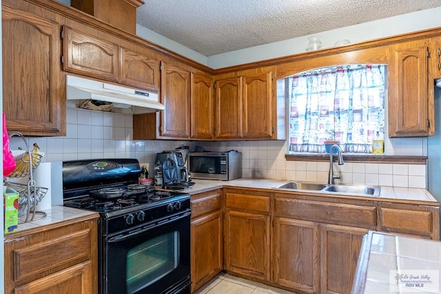 3053 Fairfield Dr, Brownsville, TX 78526 - kitchen featuring black range with gas stovetop, stainless steel microwave, tile counters, under cabinet range hood, and decorative backsplash