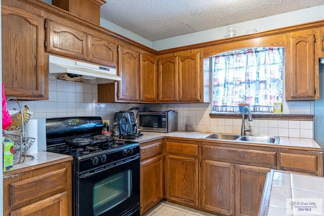 3053 Fairfield Dr, Brownsville, TX 78526 - kitchen featuring black range with gas stovetop, stainless steel microwave, tile counters, under cabinet range hood, and decorative backsplash
