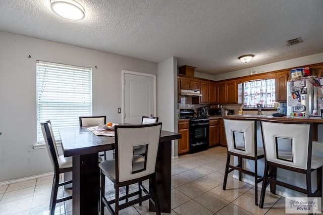 3053 Fairfield Dr, Brownsville, TX 78526 - kitchen with appliances with stainless steel finishes, under cabinet range hood, a textured ceiling, brown cabinets, and light tile patterned floors