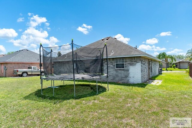 3053 Fairfield Dr, Brownsville, TX 78526 - back of house featuring a trampoline, a yard, and brick siding