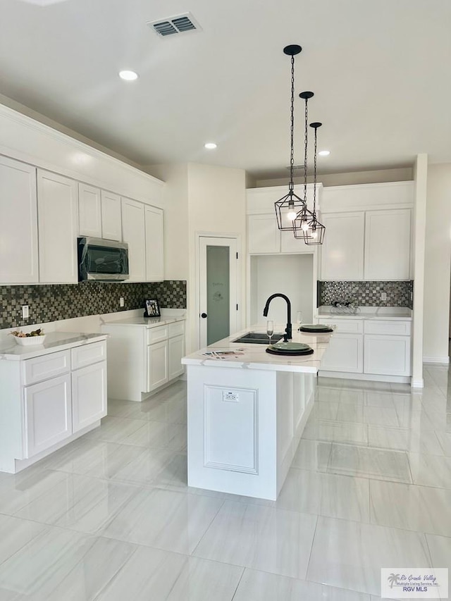 kitchen with visible vents, white cabinetry, light countertops, stainless steel microwave, and a center island with sink