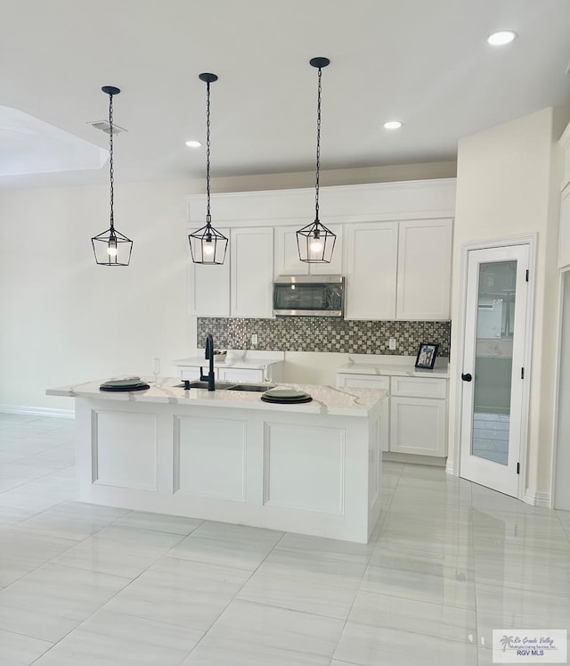 kitchen featuring a kitchen island with sink, stainless steel microwave, a sink, and decorative light fixtures