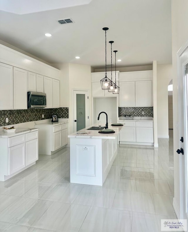 kitchen with light countertops, stainless steel microwave, a center island with sink, and white cabinetry