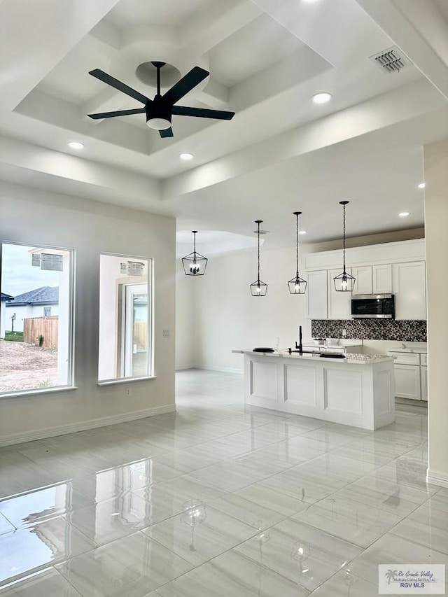 kitchen featuring a center island with sink, white cabinets, stainless steel microwave, light countertops, and pendant lighting