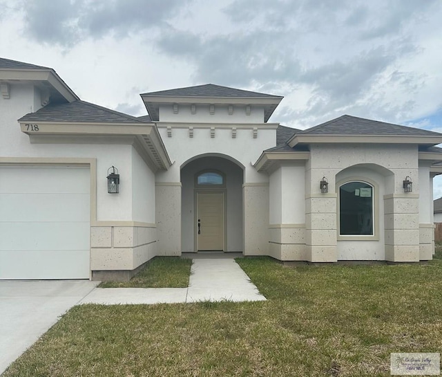 view of exterior entry with an attached garage, a shingled roof, a lawn, and stucco siding