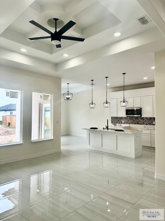 kitchen with an island with sink, stainless steel microwave, pendant lighting, and light countertops