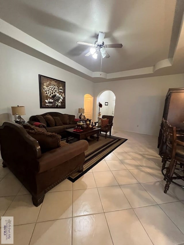 living room featuring light tile patterned floors, arched walkways, a ceiling fan, and a raised ceiling