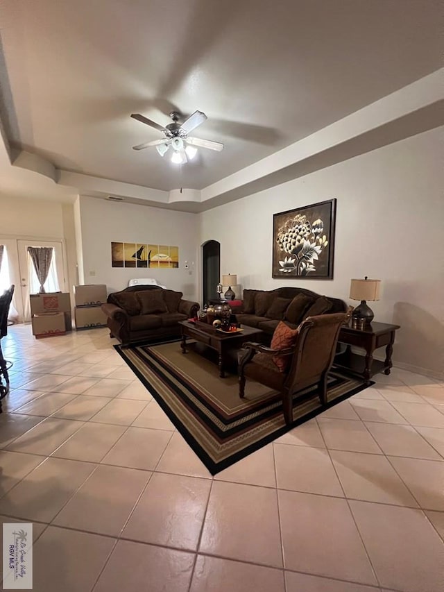 living area featuring a raised ceiling, ceiling fan, arched walkways, and light tile patterned flooring