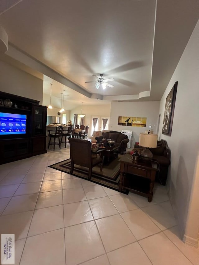 living area with tile patterned floors, ceiling fan, and a tray ceiling