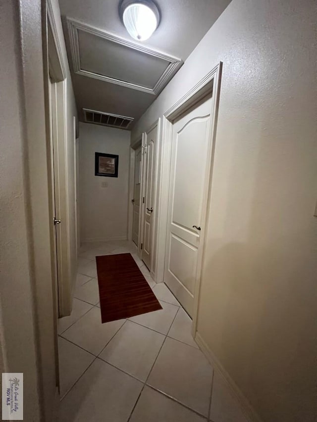 hall with visible vents, light tile patterned floors, and attic access