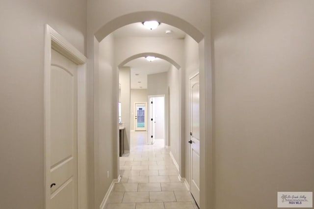 corridor with light tile patterned floors, arched walkways, and baseboards