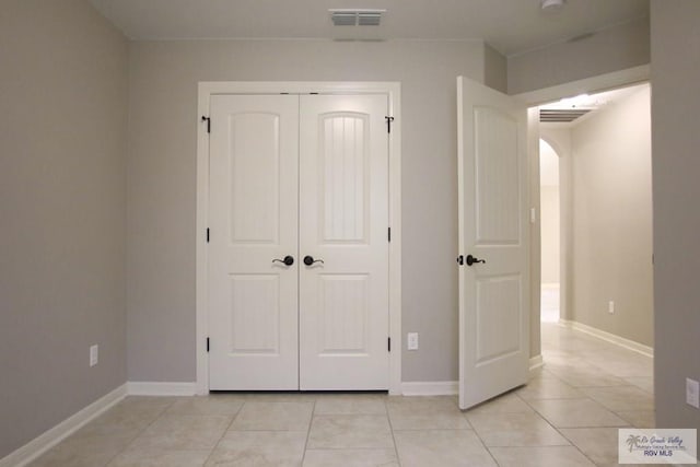 unfurnished bedroom featuring light tile patterned floors, visible vents, arched walkways, and a closet