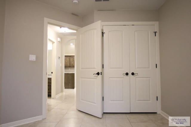 corridor with visible vents, baseboards, and light tile patterned floors