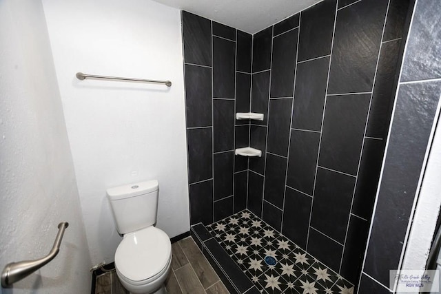 full bathroom with wood tiled floor, baseboards, a tile shower, and toilet