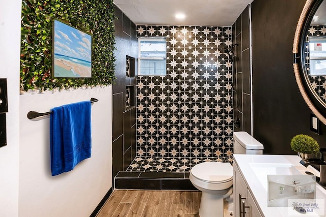 full bathroom with a tile shower, vanity, toilet, and wood finished floors