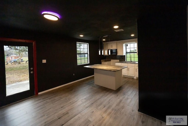 kitchen featuring decorative backsplash, white cabinets, a kitchen island, wood finished floors, and decorative light fixtures