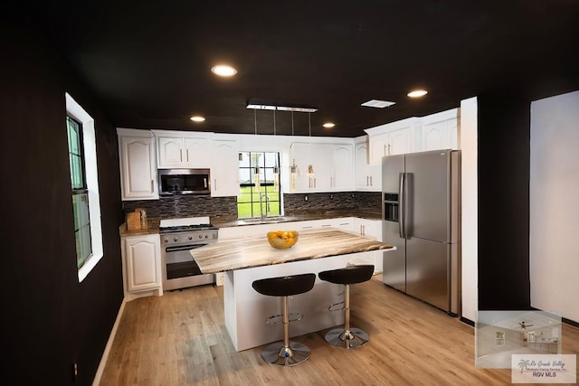 kitchen with stainless steel appliances, a sink, white cabinetry, a kitchen breakfast bar, and tasteful backsplash