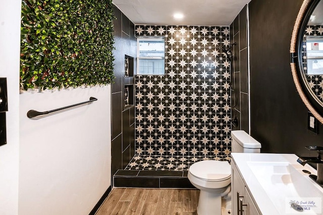 bathroom with toilet, tiled shower, wood finished floors, and vanity