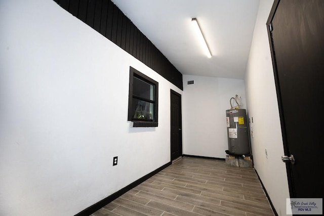 interior space featuring baseboards, water heater, visible vents, and wood finish floors