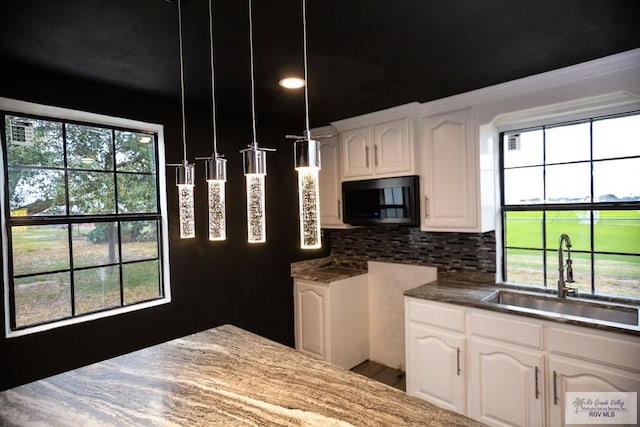 kitchen with decorative backsplash, white cabinets, a sink, and decorative light fixtures