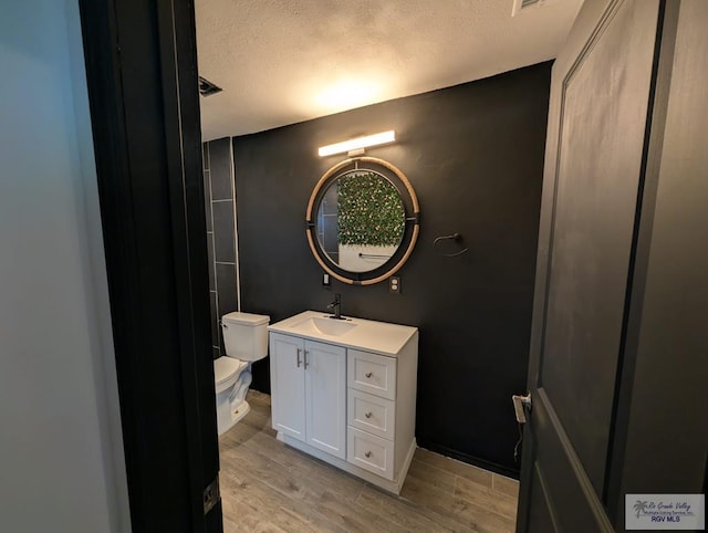 bathroom with toilet, a textured ceiling, wood finished floors, and vanity