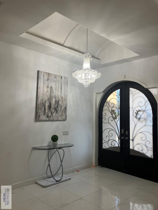 foyer entrance with a chandelier, a raised ceiling, and french doors