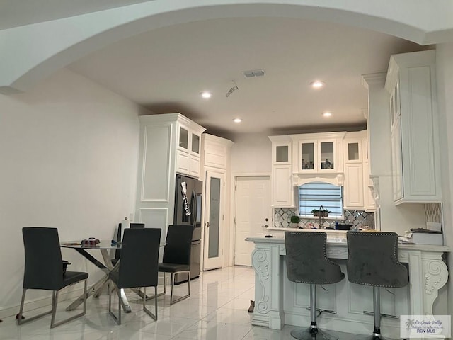 kitchen with backsplash, white cabinetry, and refrigerator