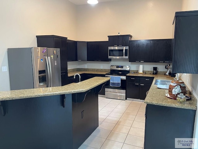 kitchen with light stone countertops, a kitchen bar, light tile patterned floors, and stainless steel appliances