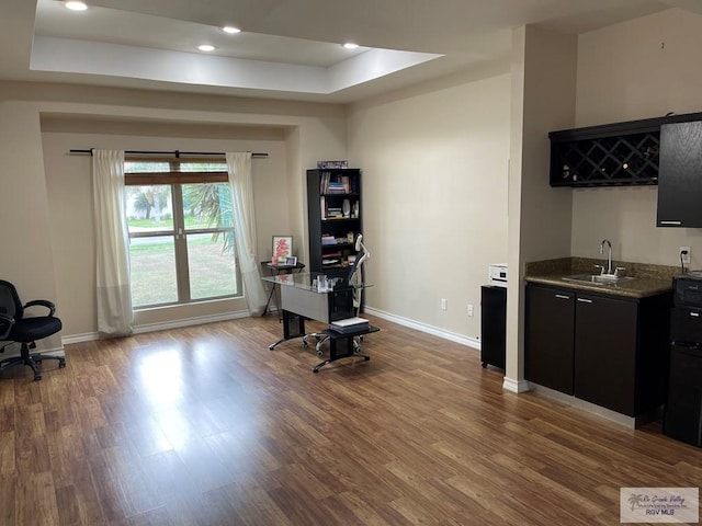 office space with a tray ceiling, hardwood / wood-style floors, and indoor wet bar