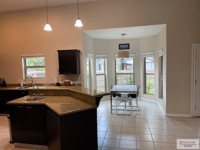 kitchen with pendant lighting, a center island with sink, sink, a towering ceiling, and light tile patterned floors