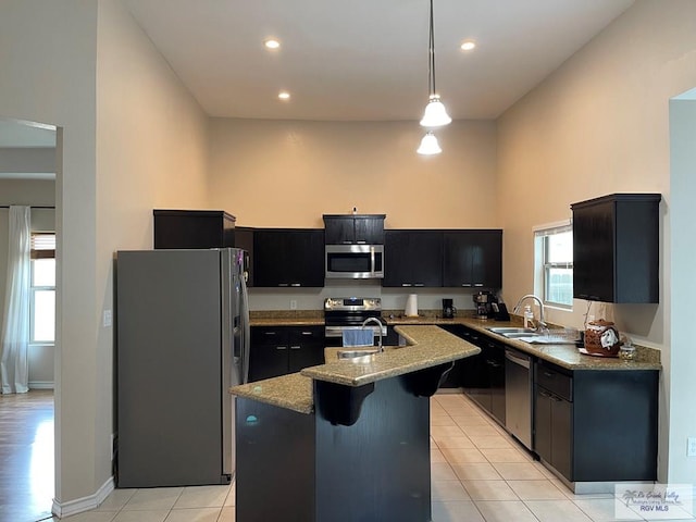 kitchen featuring sink, hanging light fixtures, stainless steel appliances, light stone counters, and a center island with sink