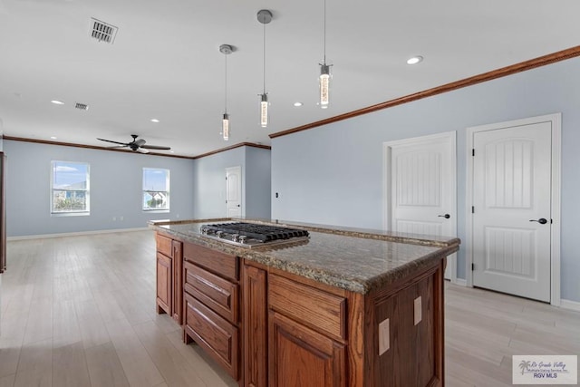 kitchen with hanging light fixtures, dark stone counters, light hardwood / wood-style flooring, a kitchen island, and stainless steel gas stovetop