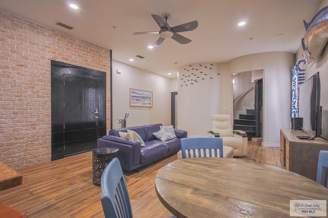 living room featuring light hardwood / wood-style floors, ceiling fan, and brick wall