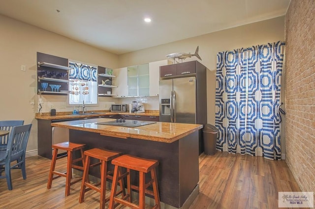 kitchen with appliances with stainless steel finishes, brick wall, sink, a center island, and dark hardwood / wood-style floors