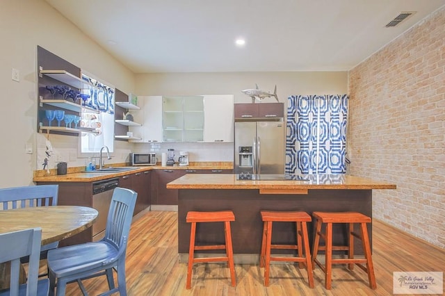 kitchen featuring sink, light wood-type flooring, a kitchen bar, stainless steel appliances, and brick wall