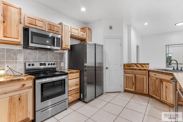 kitchen with sink, light tile patterned floors, stainless steel appliances, and light brown cabinetry