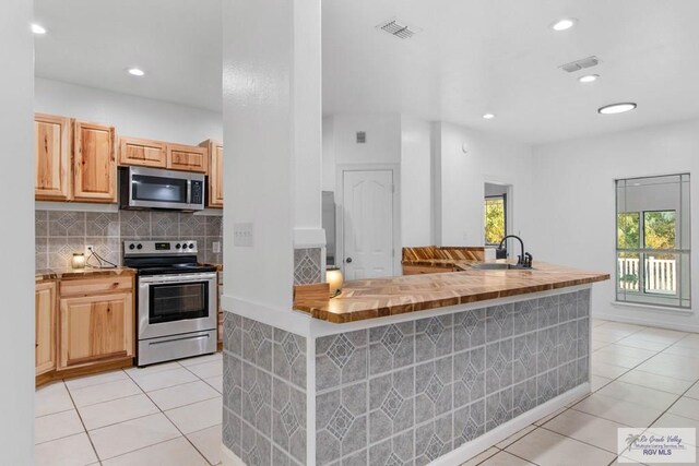 kitchen featuring sink, light tile patterned floors, light brown cabinetry, appliances with stainless steel finishes, and butcher block countertops