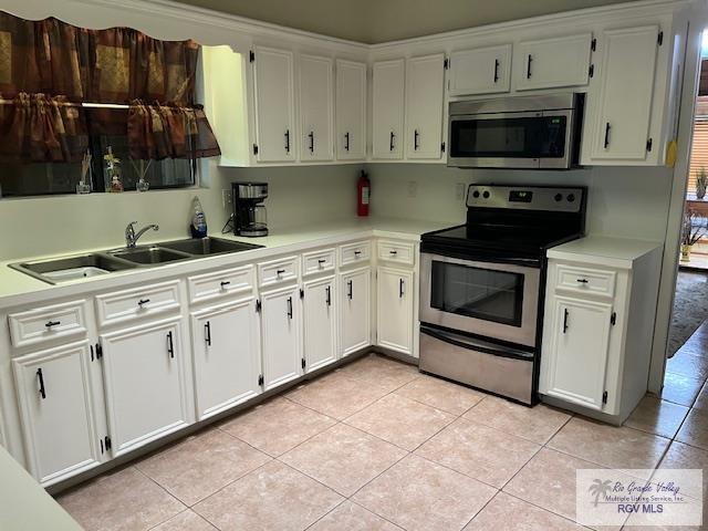 kitchen with white cabinets, appliances with stainless steel finishes, light tile patterned floors, and sink