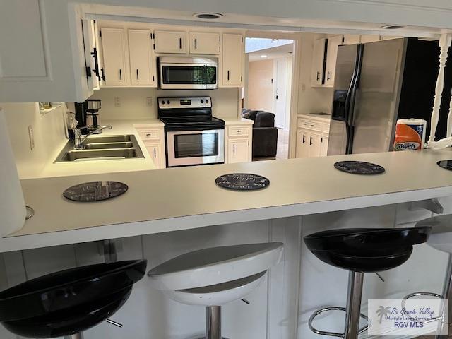 kitchen featuring a kitchen bar, white cabinetry, sink, and stainless steel appliances