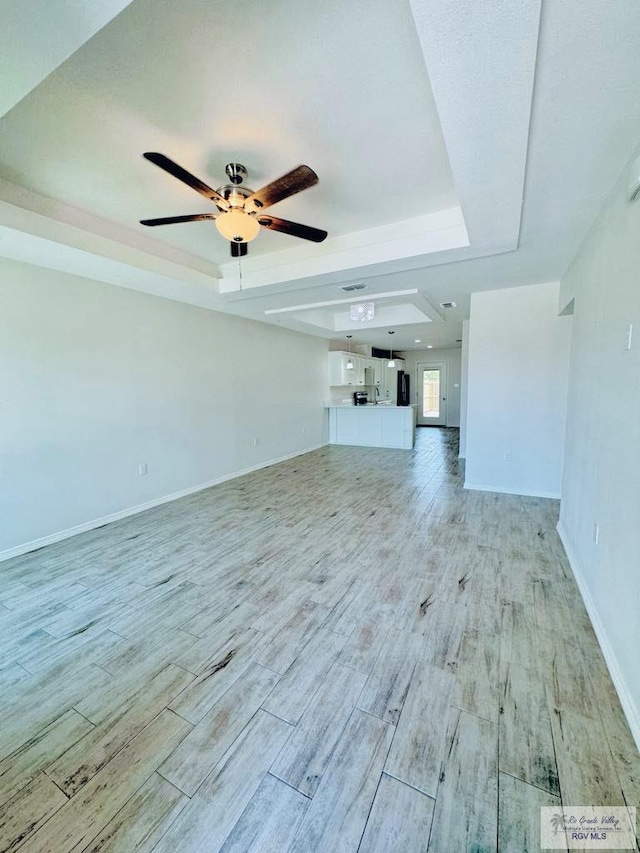 unfurnished living room with ceiling fan and a tray ceiling