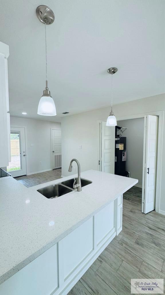 kitchen featuring decorative light fixtures, sink, white cabinetry, and light stone counters