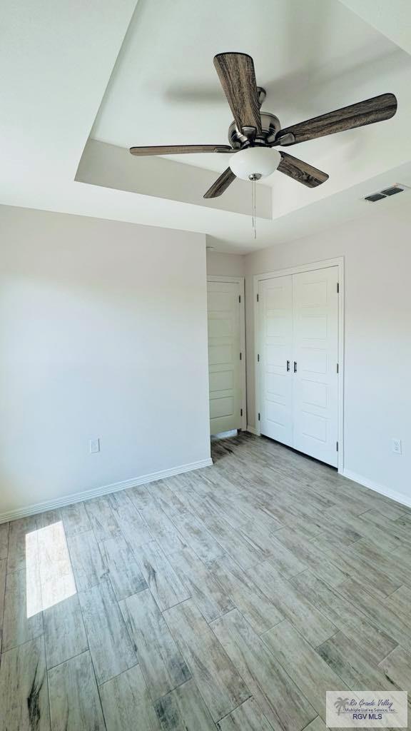 unfurnished bedroom with light wood-type flooring, a closet, a tray ceiling, and ceiling fan