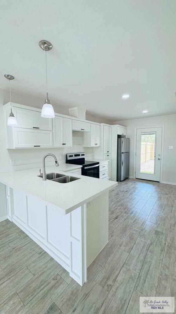 kitchen featuring white cabinetry, sink, electric stove, stainless steel fridge, and hanging light fixtures