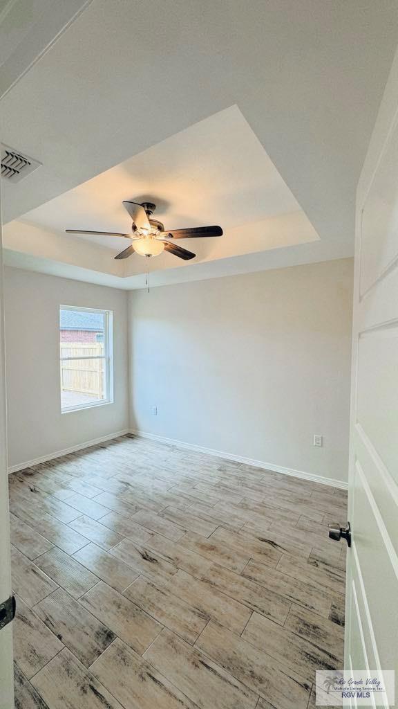 unfurnished room with ceiling fan and a tray ceiling