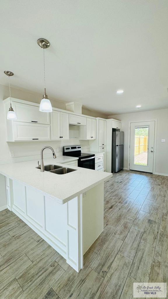 kitchen with kitchen peninsula, stainless steel fridge, sink, white cabinets, and range with electric cooktop