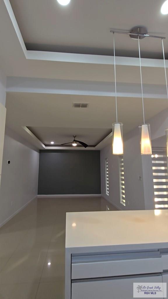 corridor featuring tile patterned floors, visible vents, baseboards, and a raised ceiling