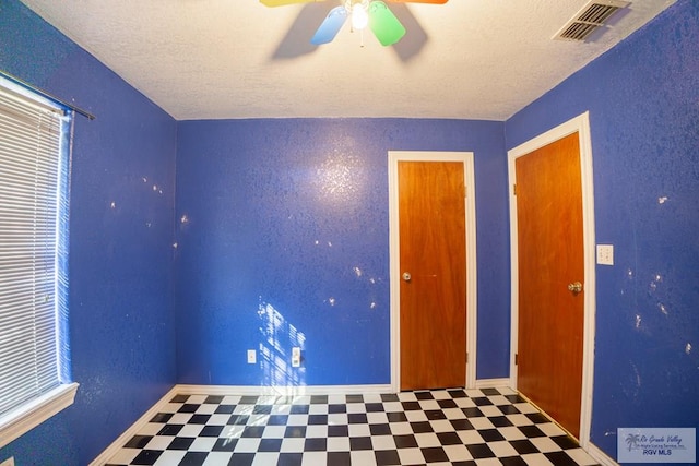 empty room with tile patterned floors, visible vents, a textured ceiling, and a ceiling fan