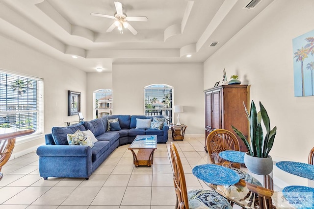 living room with light tile patterned floors, a tray ceiling, and ceiling fan