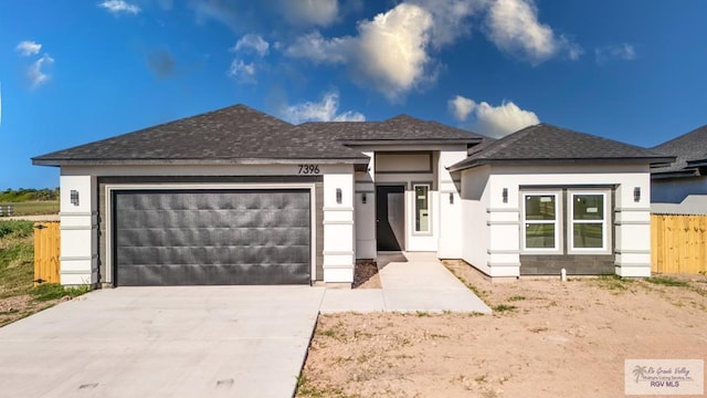 prairie-style house featuring fence, roof with shingles, stucco siding, a garage, and driveway